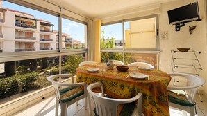 A dining area with a table set for four, chairs, a television on the wall, and a view of buildings and greenery outside.