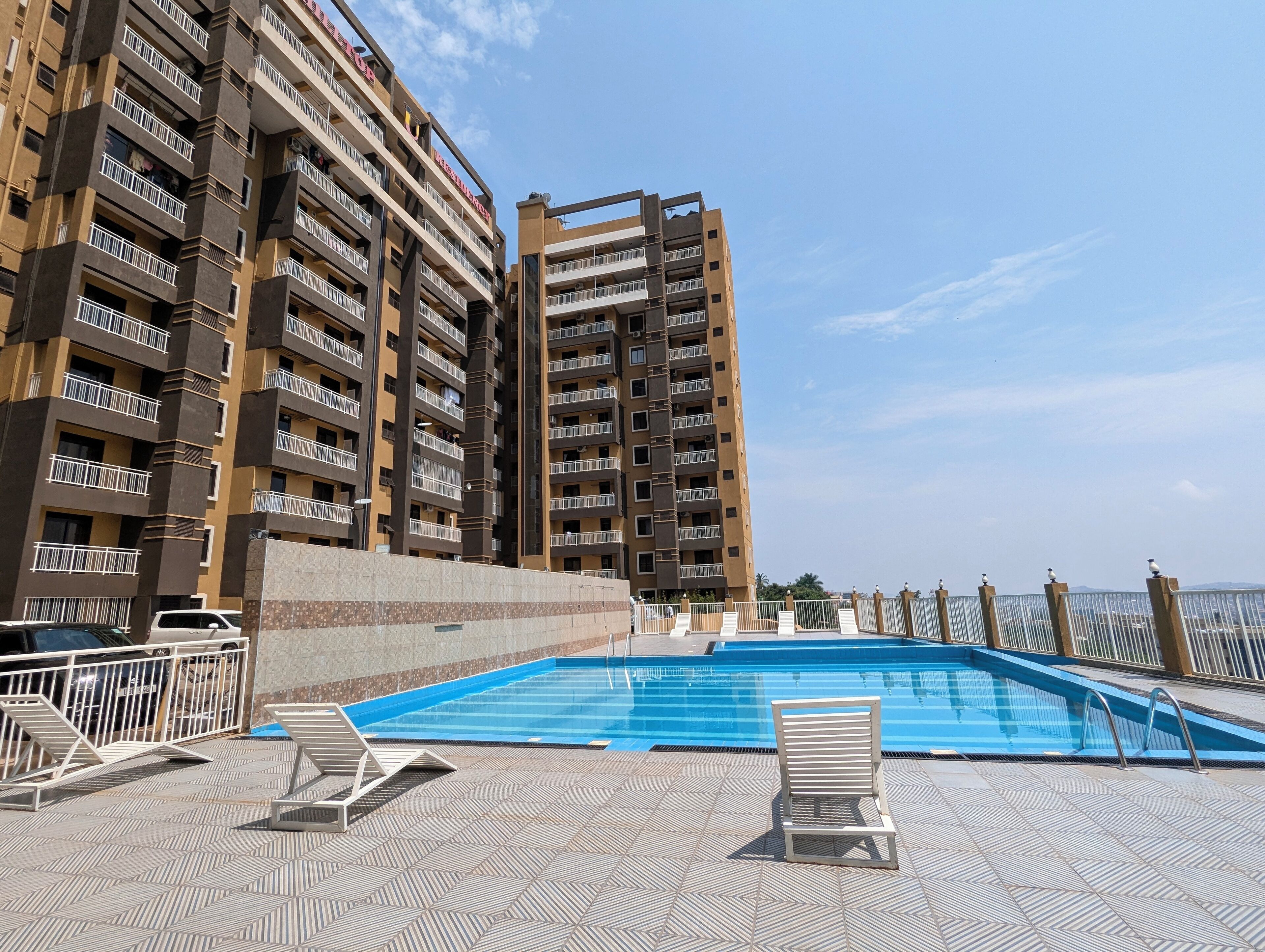 Une piscine entourée de chaises longues, elle-même bordée d’immeubles de grande hauteur dotés de balcons.