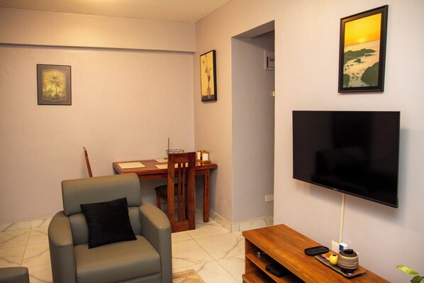 Una sala de estar con un sofá, un televisor, una mesa de comedor con sillas y cuadros en la pared.