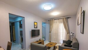 A modern living room with a flat-screen TV, grey sofas, a wooden coffee table, and a small table with a laptop. - Kololo Business Suite-Pool, Gym, fast internet/ Work, Relax & Unwind (Kampala)