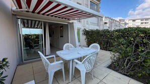 An outdoor patio with a table and chairs, a red and white awning, and a hedge. - 2-room cabin apartment, beachside, AC, private parking (Sète)
