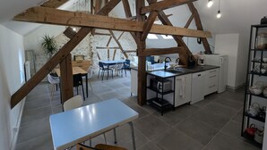 A modern kitchen with exposed wooden beams, a dining area with a table and chairs, and a view of a living room with a sofa and a plant. - Cozy room in Briare, city center, ideal for cyclists (Briare)