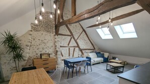 A cozy loft-style room with a wooden dining table, a sofa, and a small kitchen area. - Cozy room in Briare, city center, ideal for cyclists (Briare)