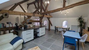 A spacious loft with exposed wooden beams, a kitchen area, a dining table with chairs, a sofa, and a coffee table. - Cozy room in Briare, city center, ideal for cyclists (Briare)