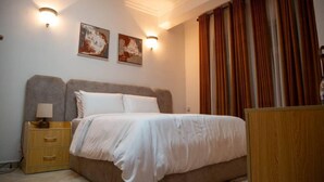 A bedroom with a bed, nightstand, lamp, and two wall-mounted lights. - Gemluxe Homes (Lagos)