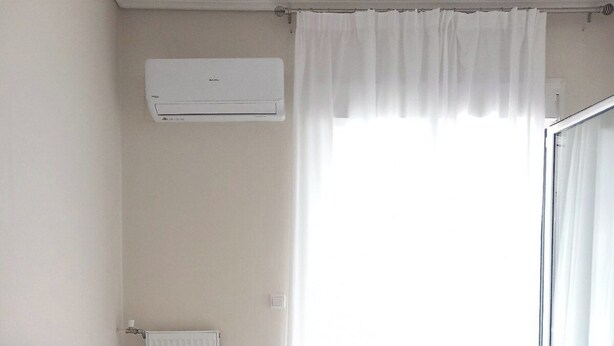 A hotel room with a bed, white bedding, a radiator, an air conditioning unit, and a window with curtains. - Koukaki Penthouse (Athens)