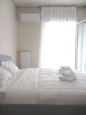 Camera d'albergo con un letto, biancheria bianca, un termosifone, un condizionatore d'aria e una finestra con tende.