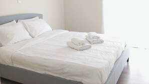 A modern hotel room with a single bed, white linens, a grey headboard, and a ceiling-mounted air conditioning unit. - Koukaki Penthouse (Athens)
