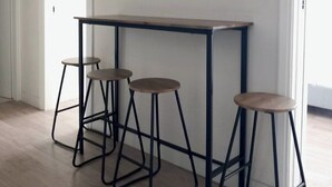A room with a wooden floor, a white door, and a white wall. There is a small table with four stools. - Koukaki Penthouse (Athens)