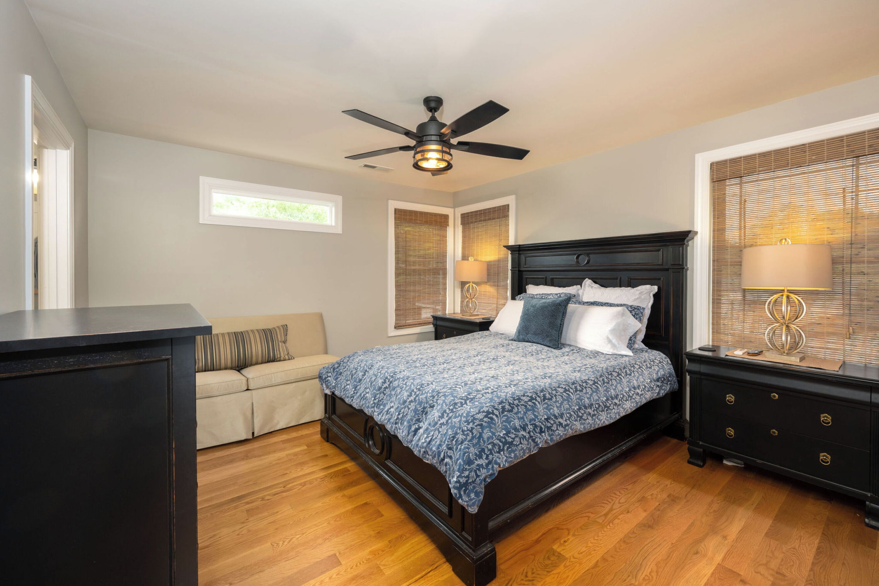 A bedroom with a bed, a ceiling fan, a nightstand, a lamp, and a window with blinds.