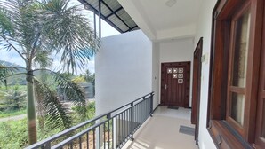 Un balcón con barandilla de metal, pared blanca y puerta de madera con detalles decorativos.