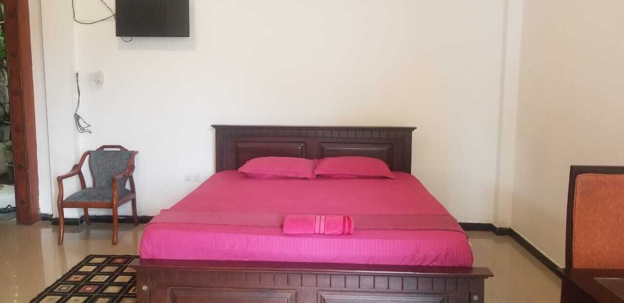 Una cama bien hecha con cabecera de madera, una silla y un televisor montado en la pared.