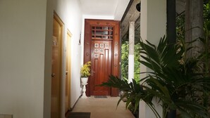 Un pasillo con una puerta de madera, una planta en maceta y una escalera que lleva al segundo piso.