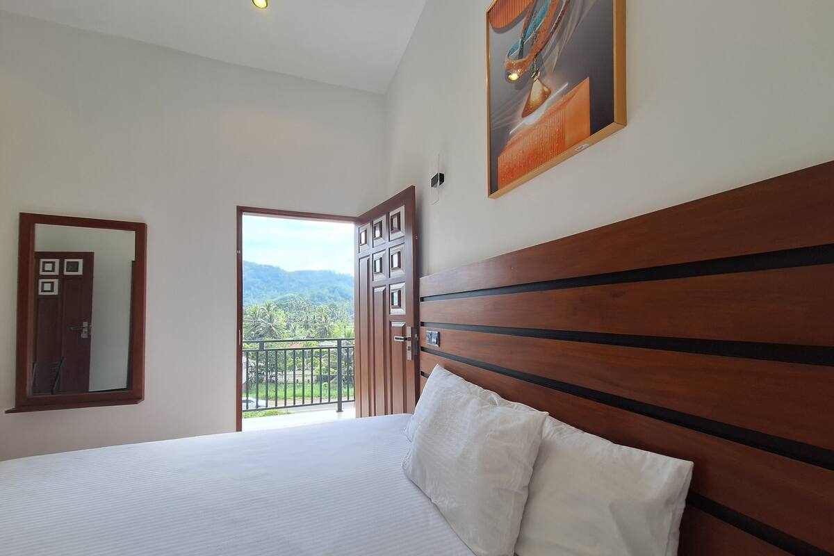 Een slaapkamer met een houten hoofdbord, een groot bed met witte lakens, een deur naar een balkon en een ingelijste foto aan de muur.