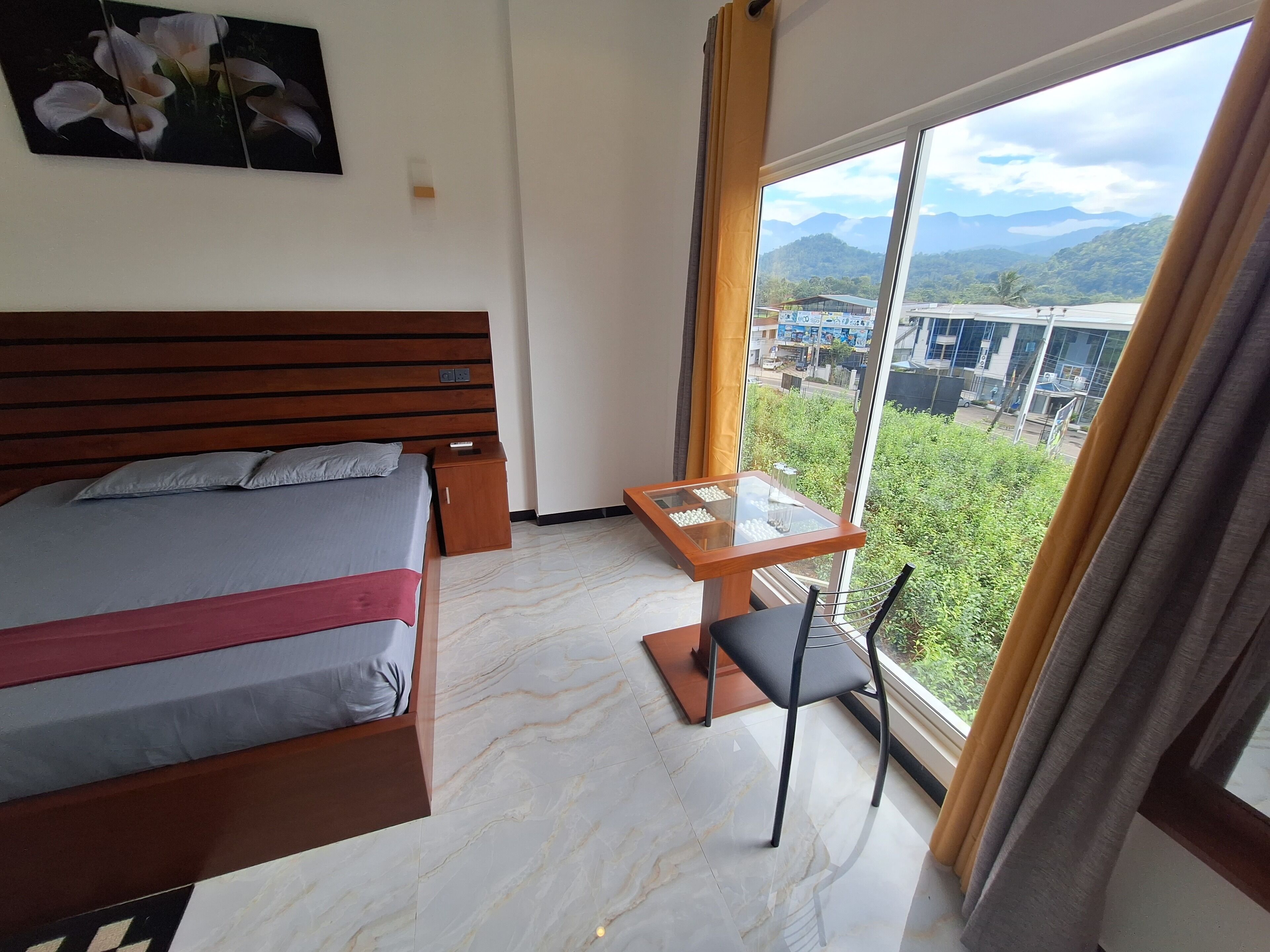 Une chambre d’hôtel avec un lit, une petite table et une chaise, ainsi qu’une grande fenêtre donnant sur la ville et les montagnes.