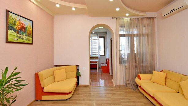 A living room with two yellow sofas, a painting on the wall, and a plant.