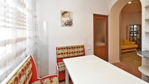 A room with a white table, a bench with a polka dot cushion, a wooden door, and a yellow sofa in the background.