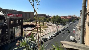 A cityscape with a prominent building featuring a red and white logo, a wide street with cars, and a clear blue sky.
