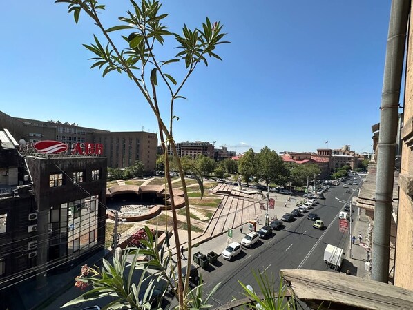 Un paisaje urbano con un edificio destacado que muestra un logotipo rojo y blanco, una calle amplia con coches y un cielo azul despejado.