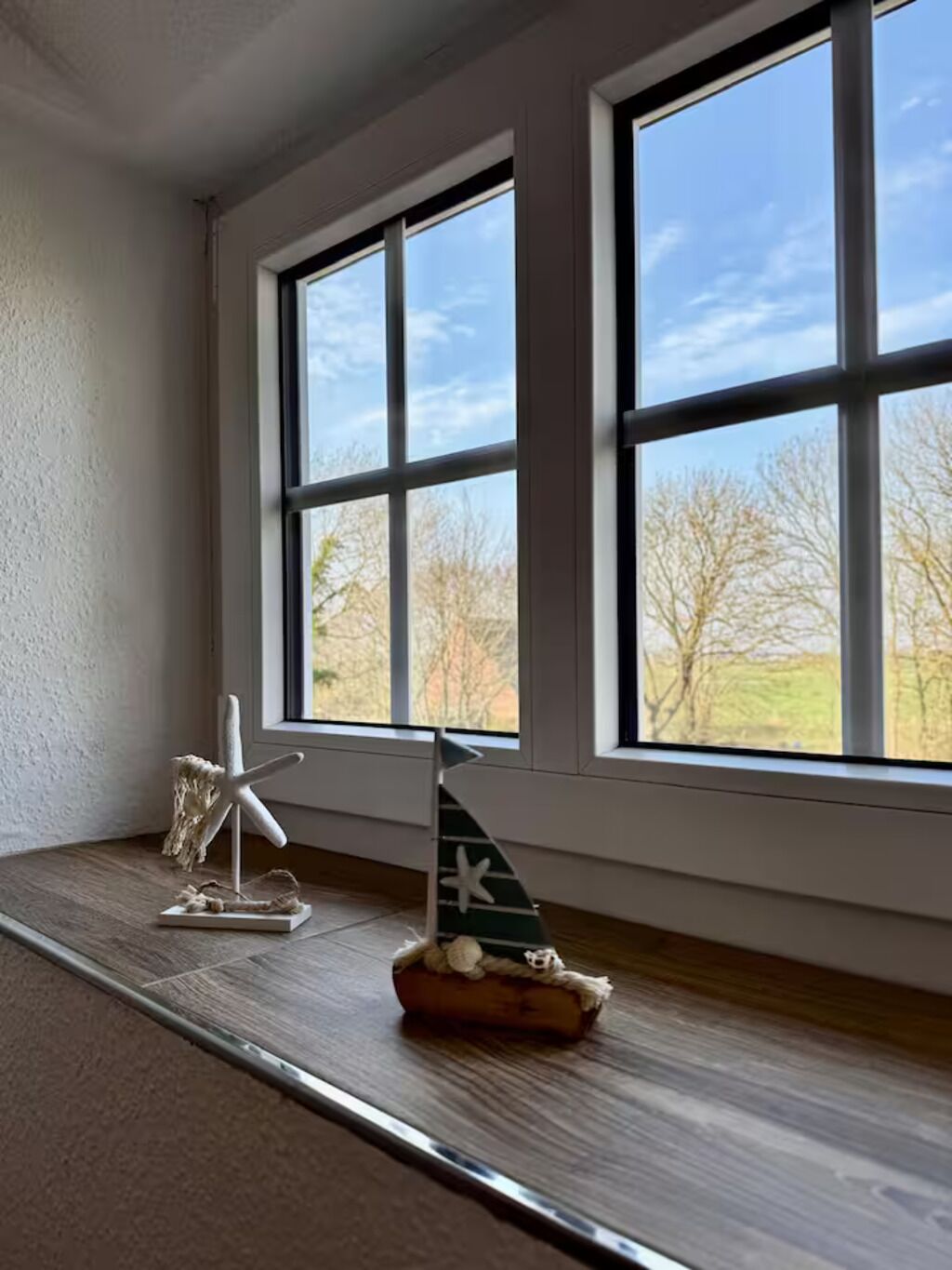 Ein Zimmer mit großen Fenstern, einer Meeressterne als Dekoration und einem kleinen Modell eines Segelbootes auf einem Holzregal.