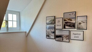 Una habitación con techo inclinado, ventana con vistas y una pared decorada con cuadros y una planta en maceta.