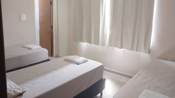 Ein Hotelzimmer mit zwei Einzelbetten, einem Badezimmer mit Duschvorhang und einer Tür zu einem weiteren Raum.