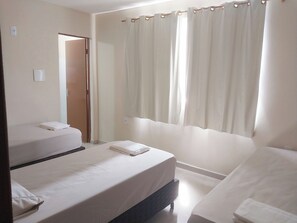 A hotel room with two single beds, a bathroom with a shower curtain, and a door leading to another room. - HOTEL HAWAII (Campos)