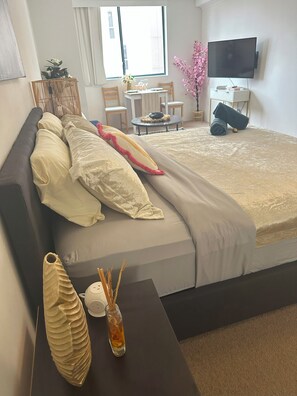 A neatly arranged hotel room with a bed, bedside table, and a small sitting area with a table and chairs. - Homely large studio with WiFi, gym pool & hot tub in vibrant Haymarket (Haymarket)