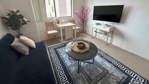 A living room with a sofa, a coffee table, a TV, a dining table with chairs, and a window with blinds.