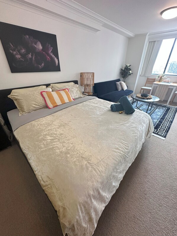 A bedroom with a large bed, a bedside table, a chair, a small table, and a window. - Homely large studio with WiFi, gym pool & hot tub in vibrant Haymarket (Haymarket)