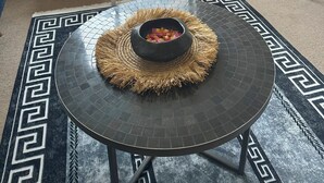 A dining area with a round table, two chairs, a vase with flowers, and a window with a view of buildings.