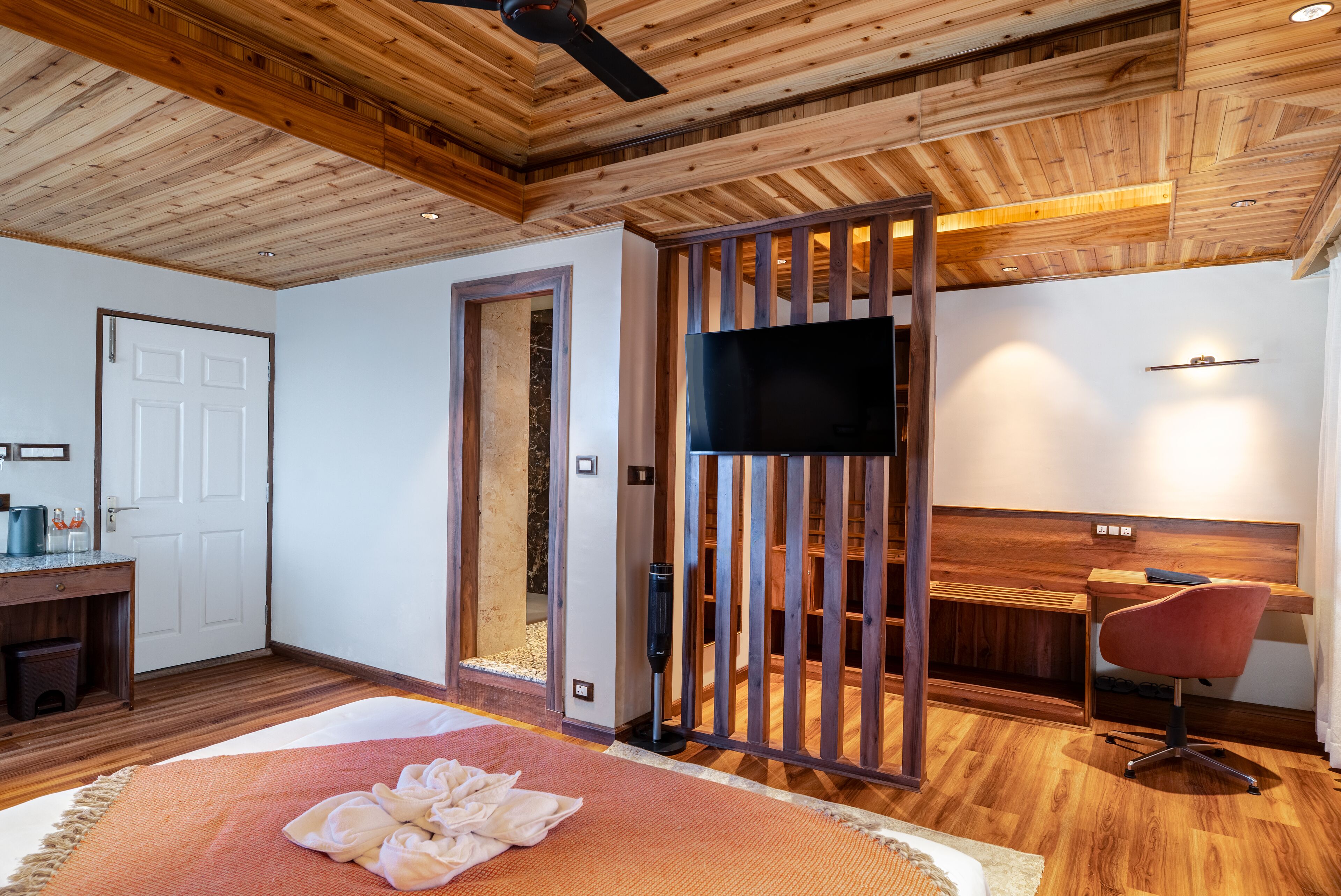 A modern bedroom with a wooden ceiling, a bed with a red and white rug, a desk with a chair, and a TV mounted on the wall.