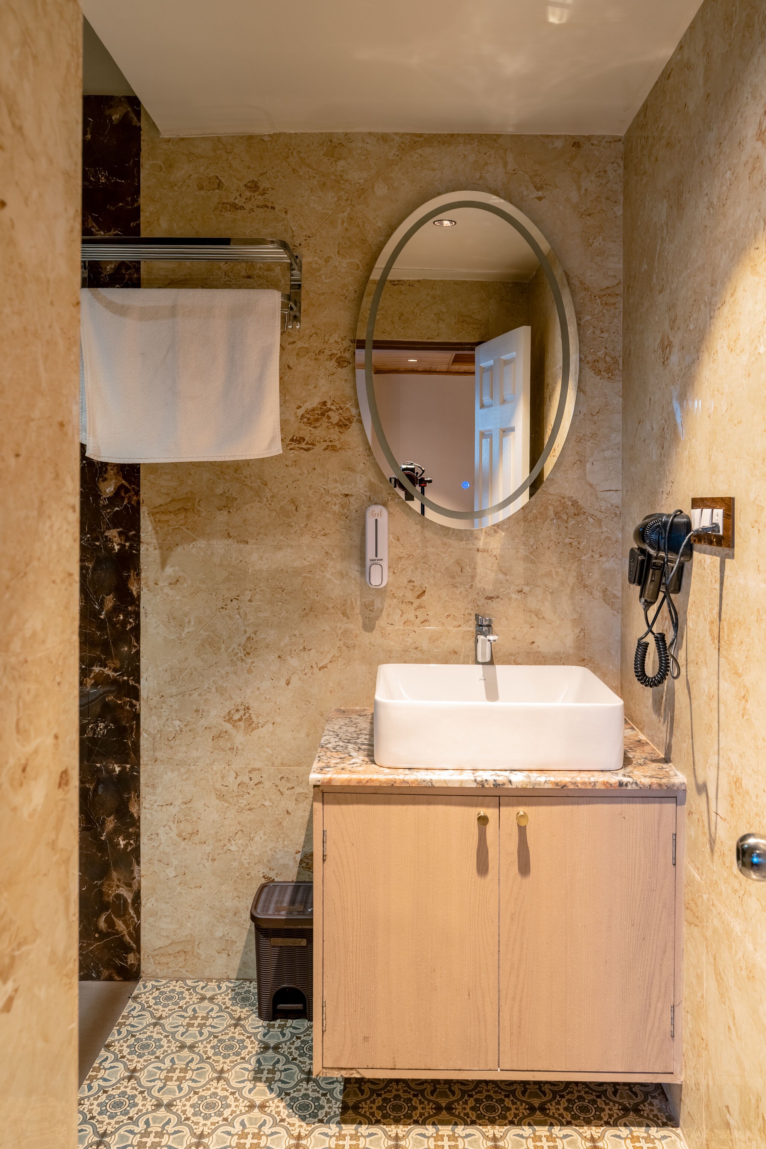 A bathroom with a marble wall, a sink with a mirror, a towel rack, and a hairdryer.