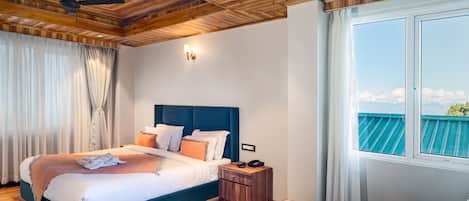 Un dormitorio con una cama grande, techo de madera, una mesita de noche, una mesa y vista al cielo a través de una ventana.