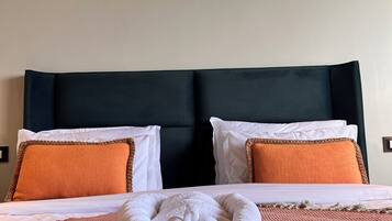 A neatly made bed with a white and orange blanket, two white pillows, and an orange throw pillow. A white towel is placed on the bed.