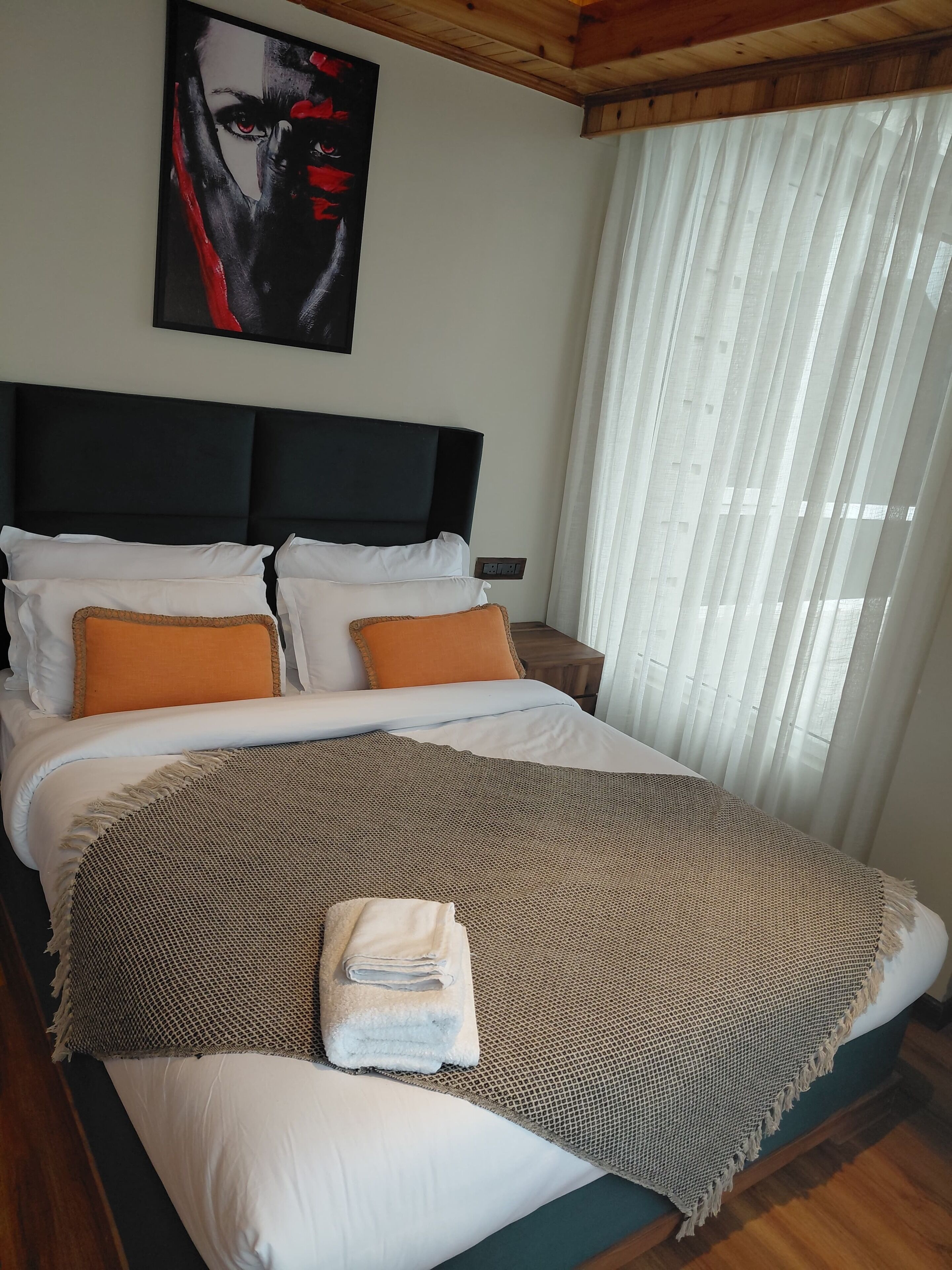 Ein ordentlich gemachtes Bett mit weißen und orangefarbenen Kissen, einer braunen, gemusterten Decke und einem gefalteten Handtuch.