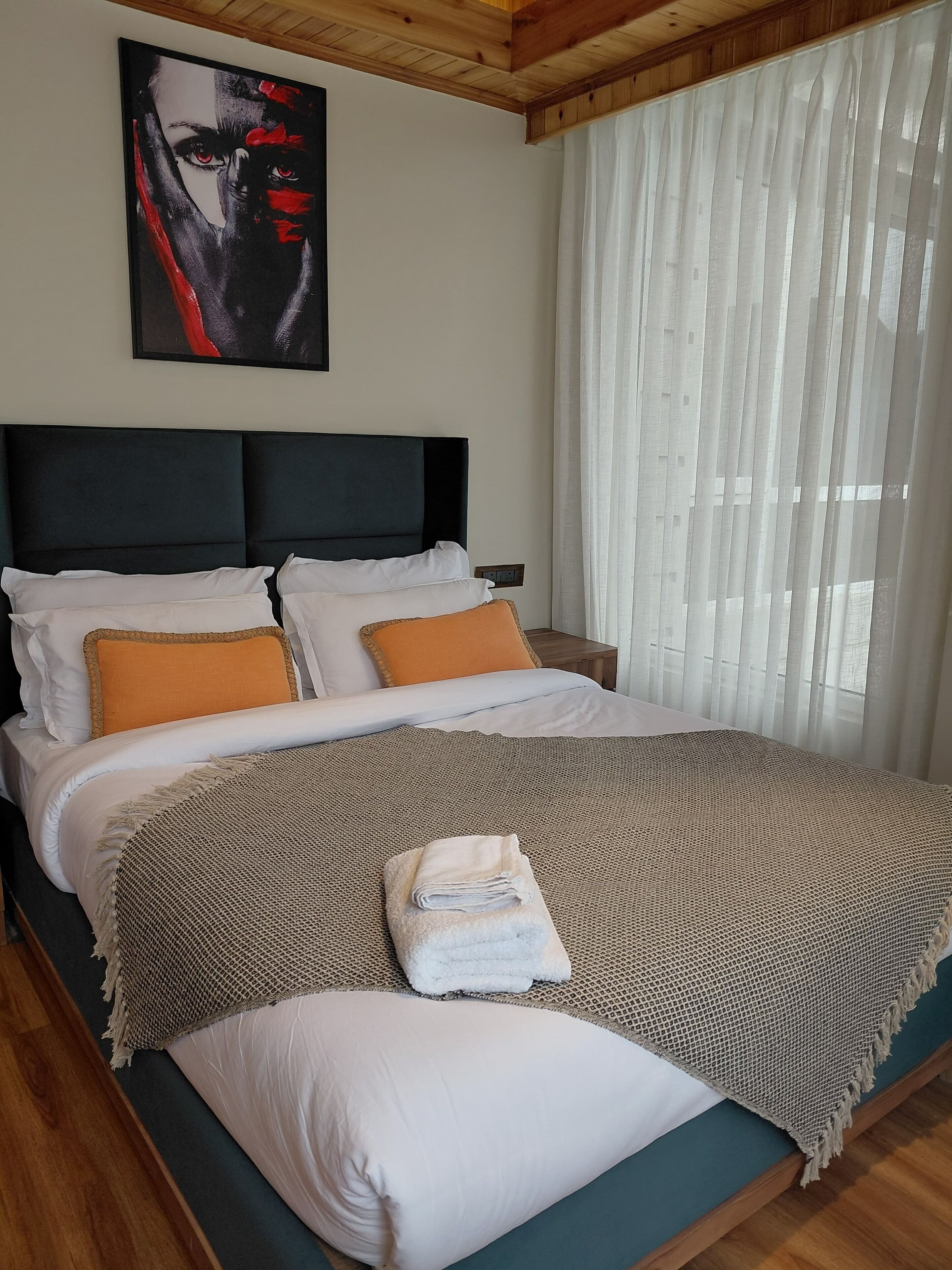 A neatly made bed with a headboard, white and orange pillows, and a folded towel.