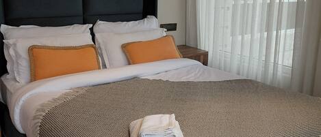 A neatly made bed with a headboard, white and orange pillows, and a folded towel.