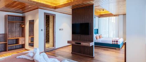 A modern bedroom with a large bed, a TV, wooden flooring, and built-in storage.