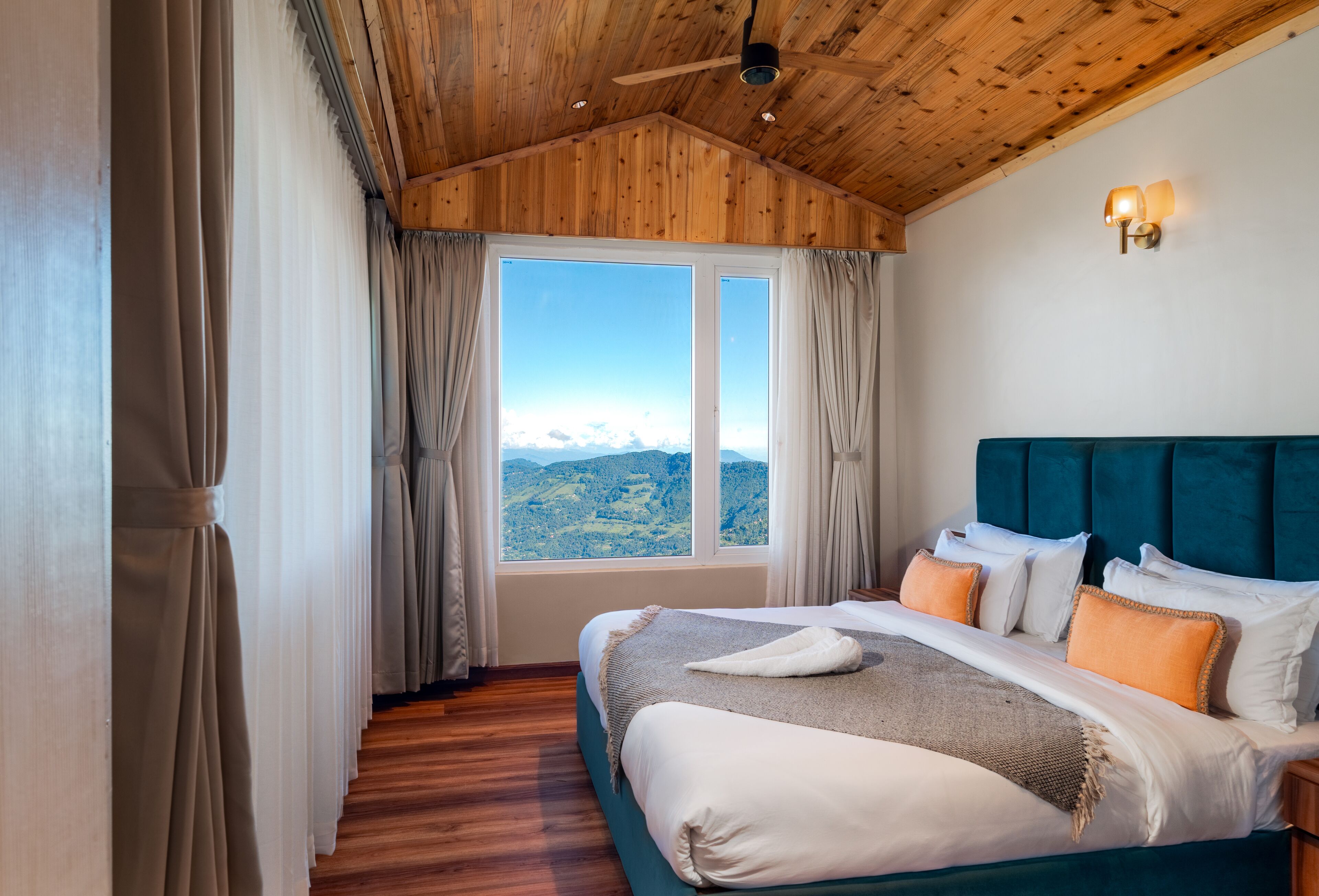 A bedroom with a large bed, wooden ceiling, and a view of the mountains through the window.