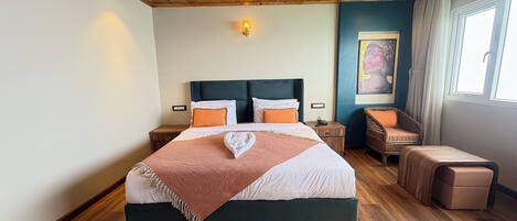 A bedroom with a wooden ceiling, a bed with white and orange bedding, a nightstand, a wicker chair, and a window with curtains.