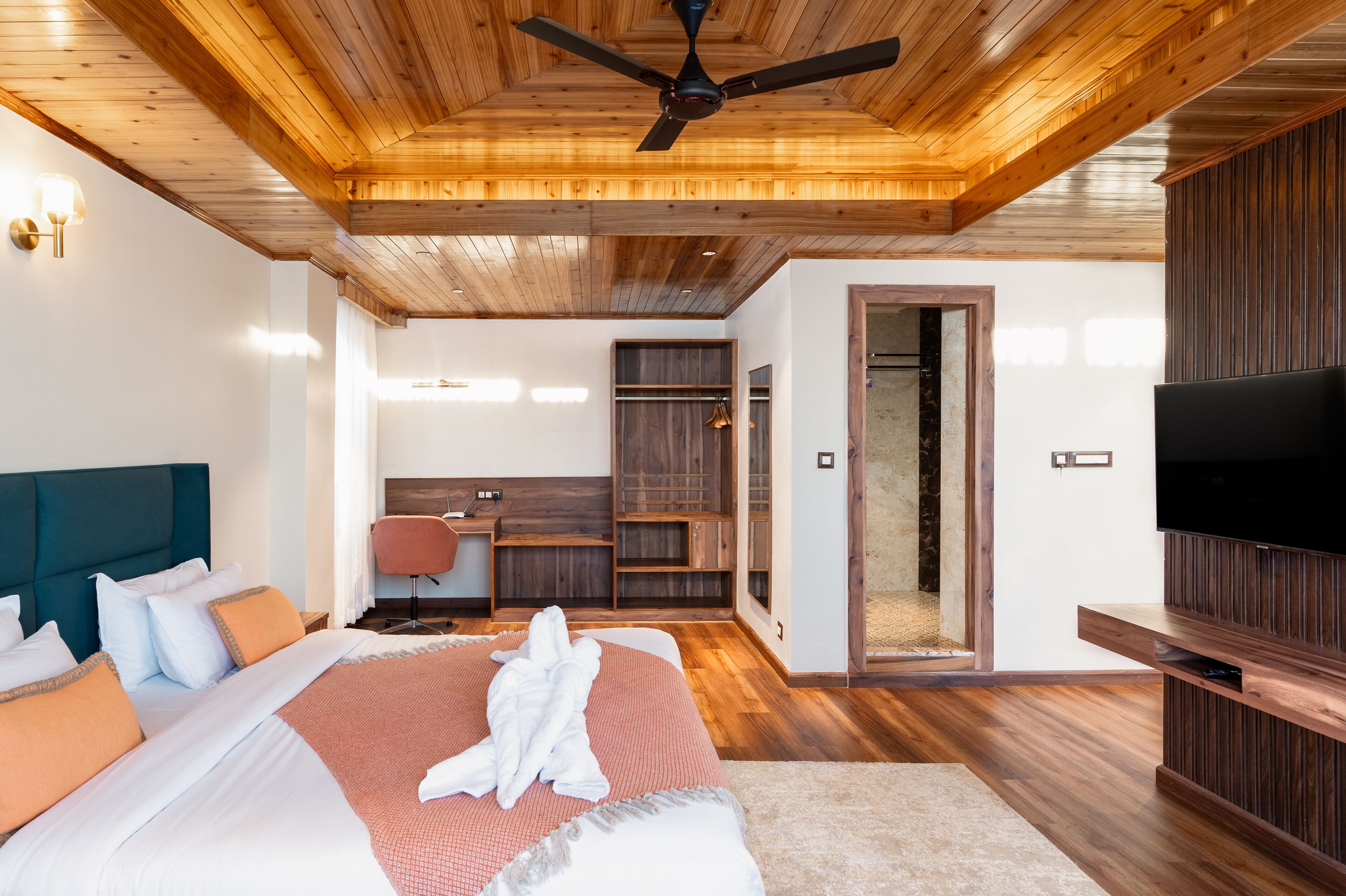 A modern bedroom with a large bed, wooden ceiling, built-in wardrobe, and a TV.