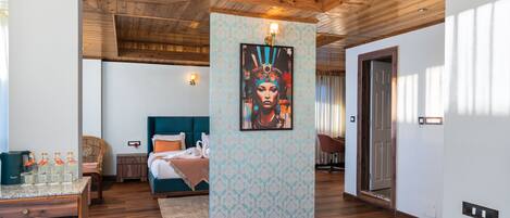 Habitación de hotel con techo de madera, cama con ropa de cama color turquesa, obra de arte colgada en la pared y escritorio con botellas.