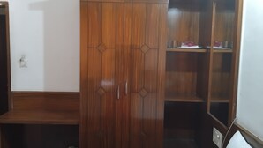 A wooden wardrobe with a mirrored door, a wooden bench, and a glass-fronted cabinet with shelves.