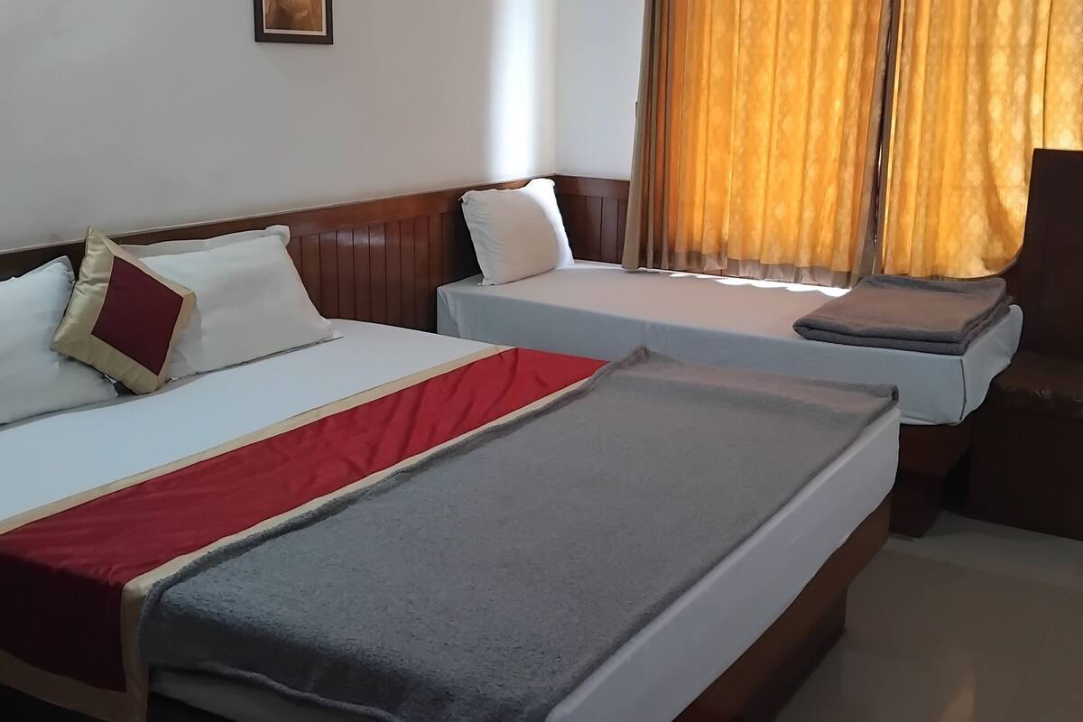 Habitación de hotel con dos camas individuales, un sofá y una ventana con cortinas.