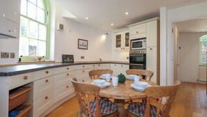 Una cocina con armarios blancos, una mesa de comedor de madera con sillas y un ventanal con vistas a la vegetación.