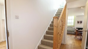 Una escalera con barandillas de madera y alfombra a rayas que conduce a una habitación con una mesa de comedor y sillas.
