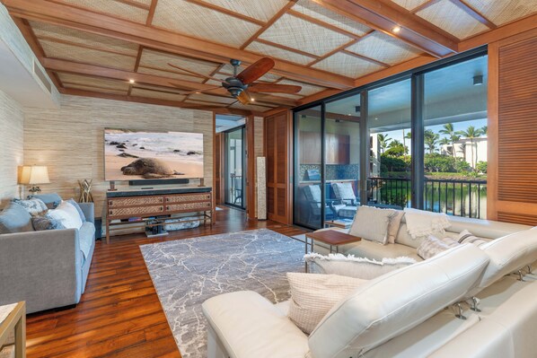 A spacious living room with a large TV, wooden ceiling, and a view of the outdoors. - 1BR-Beautiful Ground Floor, Ocean View, Mauna Lani Resort (Kamuela)