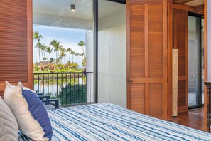 A bedroom with a large bed, a view of palm trees and a lake, and a sliding door to a balcony. - 1BR-Beautiful Ground Floor, Ocean View, Mauna Lani Resort (Kamuela)