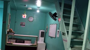 A room with teal walls, a desk with a computer, a small fan, a clock, and a staircase. - WIND STAY Guest House (Malé)